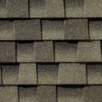 Close-up view of overlapping dark gray asphalt roof shingles arranged in a staggered pattern, showing their rough, textured surface.