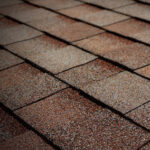 Close-up view of overlapping brown asphalt roof shingles, arranged in neat horizontal rows, displaying a rough, textured surface.