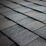 Close-up view of dark gray asphalt roof shingles arranged in a neat, overlapping pattern, creating a textured surface.