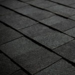 Close-up view of dark gray asphalt roof shingles arranged in neat, overlapping rows, showing texture and pattern.
