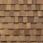 Close-up view of a pattern of brown asphalt roof shingles, arranged in overlapping rows with varying shades of tan and brown.
