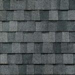 Close-up view of a roof covered with overlapping rectangular dark gray asphalt shingles arranged in neat, horizontal rows. The surface has a rough, textured appearance.