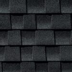 Close-up view of dark gray asphalt roof shingles arranged in a staggered pattern, showing coarse, textured surfaces with visible granules.