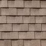Close-up view of a roof covered with overlapping rectangular brown asphalt shingles, arranged in a neat, horizontal pattern.