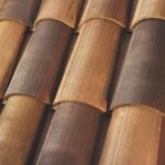 Close-up view of overlapping, curved terracotta roof tiles in various shades of brown and tan, forming a textured and patterned surface.