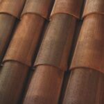 Close-up view of overlapping brown terracotta roof tiles arranged in neat rows, showing their curved shapes and textured surfaces.