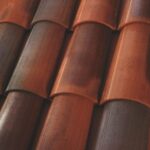 Close-up of overlapping red and brown ceramic roof tiles arranged in a repeating pattern, showing their curved, textured surfaces and slight color variations.