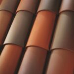 A close-up view of overlapping roof tiles in shades of brown and reddish-orange, arranged in a neat, repeating pattern.