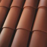 Close-up view of overlapping reddish-brown clay roof tiles arranged in neat, parallel rows, showing their curved, traditional design.