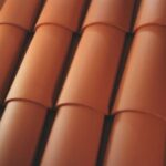 Close-up view of overlapping, curved terracotta roof tiles arranged in neat, horizontal rows. The tiles have a smooth surface and a rich, reddish-orange color.