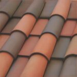 Close-up view of overlapping, curved terracotta roof tiles in alternating reddish and brownish tones, creating a textured, repeating pattern.