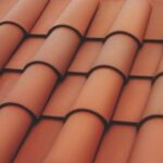Close-up view of overlapping terracotta roof tiles arranged in neat, horizontal rows, creating a textured pattern. The tiles are a reddish-brown color typical of traditional Mediterranean-style roofing.