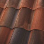 Close-up of overlapping terracotta roof tiles with a textured surface, showing a mix of reddish, brown, and dark tones in natural light.