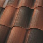 Close-up view of terracotta roof tiles with alternating ridges and grooves, showing a mix of reddish-brown and darker weathered areas.