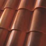 Close-up view of overlapping reddish-brown clay roof tiles, showing their curved, smooth surfaces and uniform, repeating pattern.