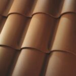 Close-up view of overlapping terracotta roof tiles, arranged in neat, parallel rows, creating a repeating, wavy pattern. The tiles have a smooth, matte finish and a warm, reddish-brown color.