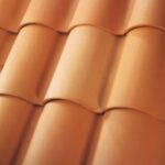 Close-up view of overlapping terracotta roof tiles arranged in a neat, uniform pattern, showing their smooth texture and curved shape.
