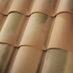 Close-up view of tan-colored, curved clay roof tiles arranged in overlapping rows, creating a wavy pattern and a smooth texture.