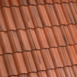 Close-up view of a roof covered with overlapping red clay tiles, arranged in neat horizontal rows with visible shadows and slight color variations.