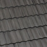 Close-up view of overlapping dark gray roof tiles arranged in a regular, horizontal pattern, showing the ridged texture and uniform alignment of the roofing material.