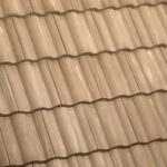 Close-up view of beige ceramic roof tiles arranged in a wavy, overlapping pattern, creating a uniform and textured surface.