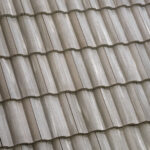 Close-up view of overlapping, wavy beige roof tiles arranged in neat horizontal rows, forming a repetitive textured pattern.