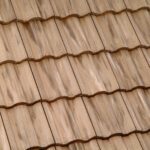 Close-up view of beige ceramic roof tiles arranged in a wavy, overlapping pattern, creating a textured surface. The tiles have slight variations in color and shading.