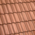 Close-up view of brown terracotta roof tiles arranged in neat, overlapping rows, creating a wavy, textured pattern.
