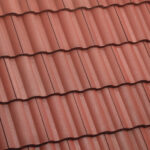 Close-up view of red, wavy roof tiles arranged in neat horizontal rows, creating a textured and uniform pattern typically seen on residential rooftops.