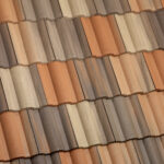 Close-up view of a tiled roof with alternating rows of brown, tan, and reddish-orange clay tiles, arranged in a wavy, overlapping pattern.