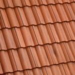 Close-up view of red clay roof tiles arranged in overlapping rows, creating a wavy, textured pattern typical for traditional roofing.
