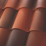 Close-up view of overlapping reddish-brown curved roof tiles, arranged in neat, horizontal rows. The smooth tiles create a textured, patterned surface typical of tiled roofing.