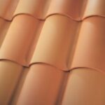 Close-up view of overlapping terracotta roof tiles with a smooth, curved surface, arranged in a wavy pattern. The tiles have a warm, orange-brown color and are neatly aligned.