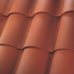 Close-up view of overlapping red clay roof tiles, arranged in neat, horizontal rows with curved, wavy shapes. The tiles have a smooth matte finish and are tightly fitted together.