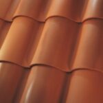 Close-up view of overlapping, curved, reddish-orange roof tiles arranged in neat horizontal rows, showing the smooth texture and glossy finish of the tiles.