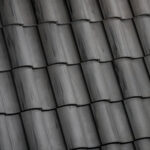 Close-up view of dark gray ceramic roof tiles arranged in overlapping rows, creating a textured and uniform pattern.
