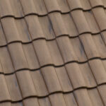 Close-up view of a roof covered with overlapping brown ceramic tiles, arranged in a wavy, repeating pattern. The tiles have a slightly weathered appearance and fit tightly together.