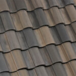Close-up view of overlapping, curved, brown and gray concrete roof tiles arranged in neat, horizontal rows, illustrating a textured pattern.