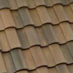 Close-up of a roof with overlapping brown ceramic tiles, showing a wavy pattern and subtle variations in color and texture.