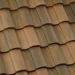 Close-up view of overlapping brown and tan ceramic roof tiles arranged in a wavy, repetitive pattern. The tiles have a textured surface and show slight variations in color and shading.