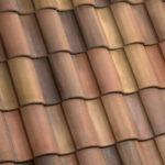 Close-up view of overlapping terracotta roof tiles in shades of brown, orange, and tan, creating a repeating wavy pattern.