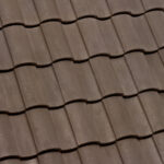 Close-up view of brown, wavy, overlapping roof tiles arranged in horizontal rows, creating a textured and uniform pattern.