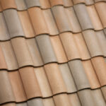 Close-up of overlapping terracotta roof tiles in shades of beige and light brown, arranged in a repeating, wavy pattern.