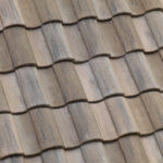 Close-up view of overlapping brown and gray clay roof tiles arranged in neat, horizontal rows, creating a textured and wavy pattern.