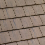 A close-up view of a rooftop with evenly arranged, overlapping rectangular brown tiles, showing their textured surface and neat alignment.