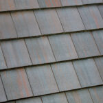 A close-up view of a roof covered with overlapping rectangular gray tiles, some showing slight reddish rust stains and weathering.