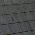 Close-up view of dark gray, rectangular roofing tiles arranged in a staggered, overlapping pattern, creating a uniform and textured surface.