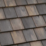 Close-up view of a roof covered with rectangular, overlapping brown and gray ceramic or concrete shingles arranged in neat horizontal rows.
