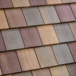 Close-up view of a rooftop covered with rectangular, overlapping tiles in varying shades of brown, beige, and muted purple, arranged in a neat, repeating pattern.