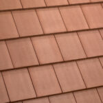 Close-up of a roof with overlapping rectangular terracotta tiles arranged in neat, horizontal rows. The tiles have a slightly textured surface and uniform color.